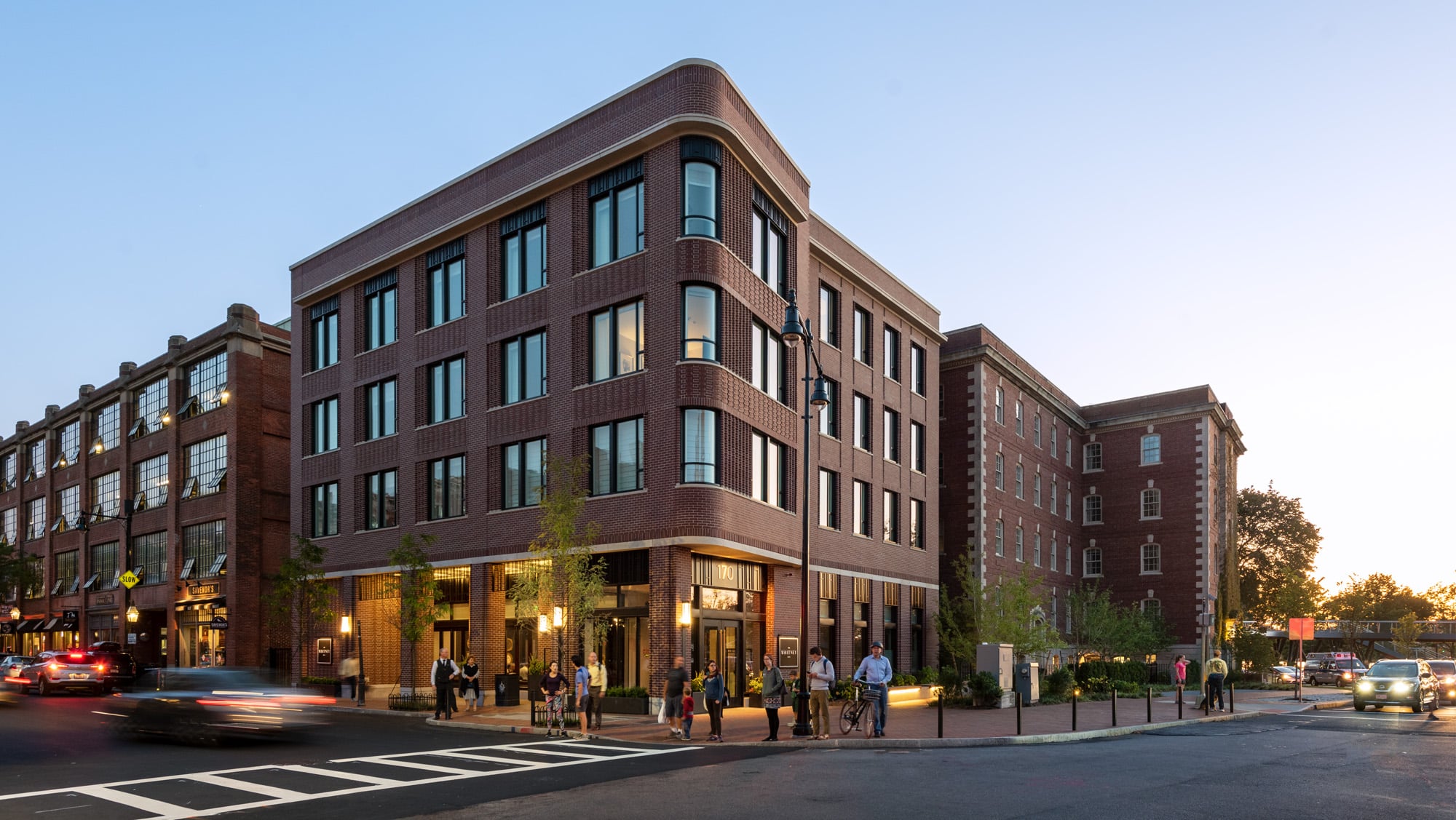 Evening view of a brick building on a bustling corner with people walking the sidewalk