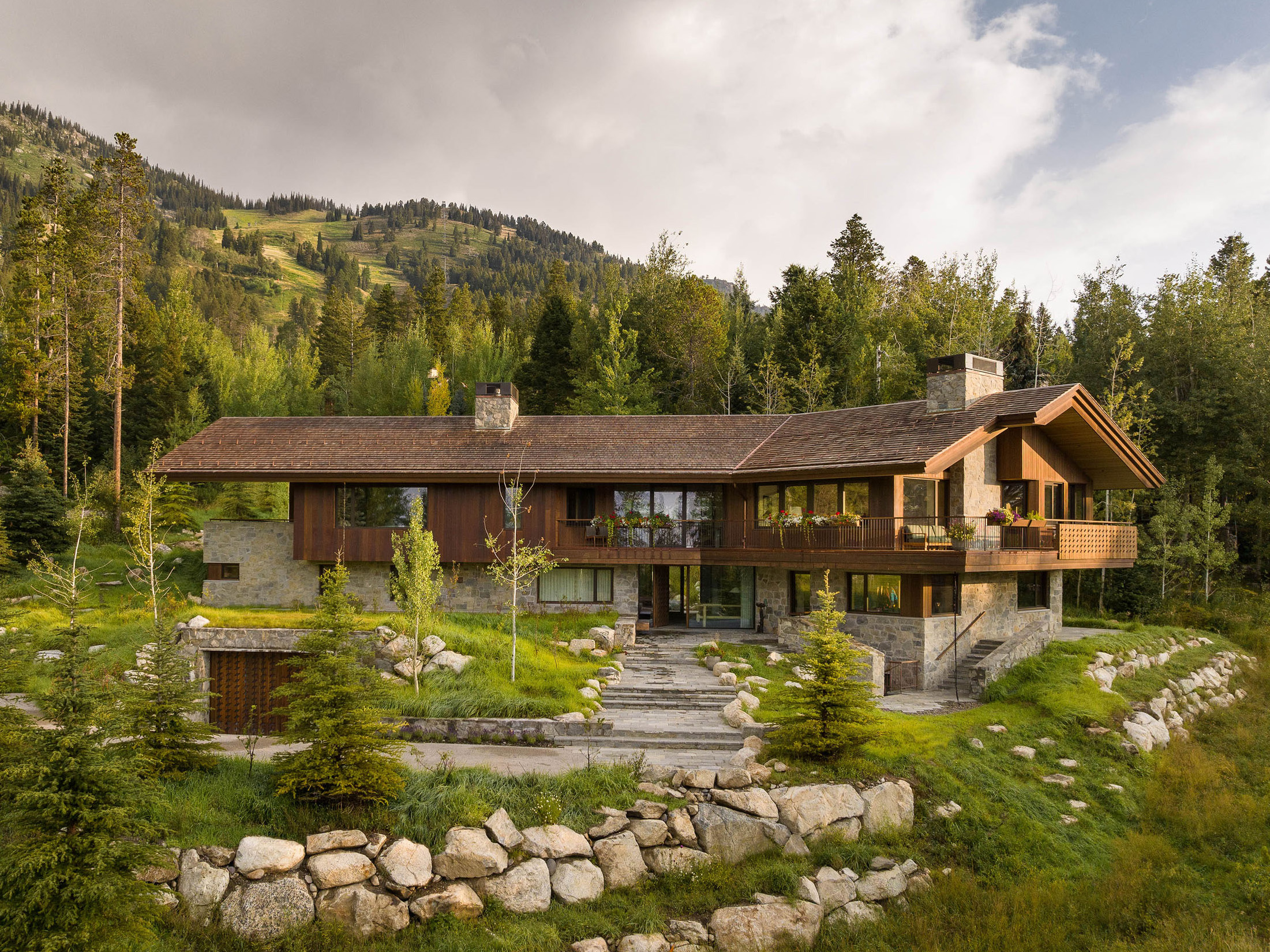 A large ski chalet in the summertime with verdant landscaping and mountains in the background.